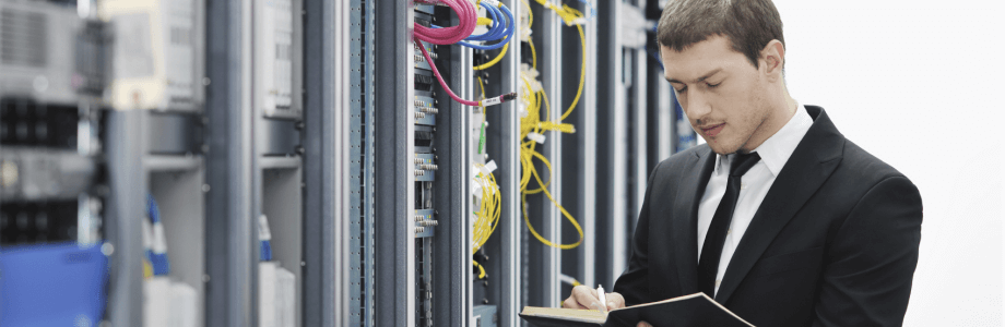 IT Controlling Interview Mann steht vor Servern und notiert sich etwas.