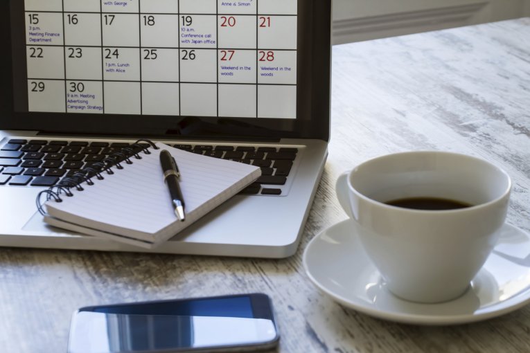 Laptop mit Kalender, Smartphone, Notizbuch und Tasse Kaffee auf Tisch