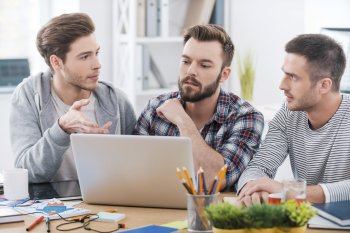 Drei Studenten sitzen um einen Laptop und diskutieren